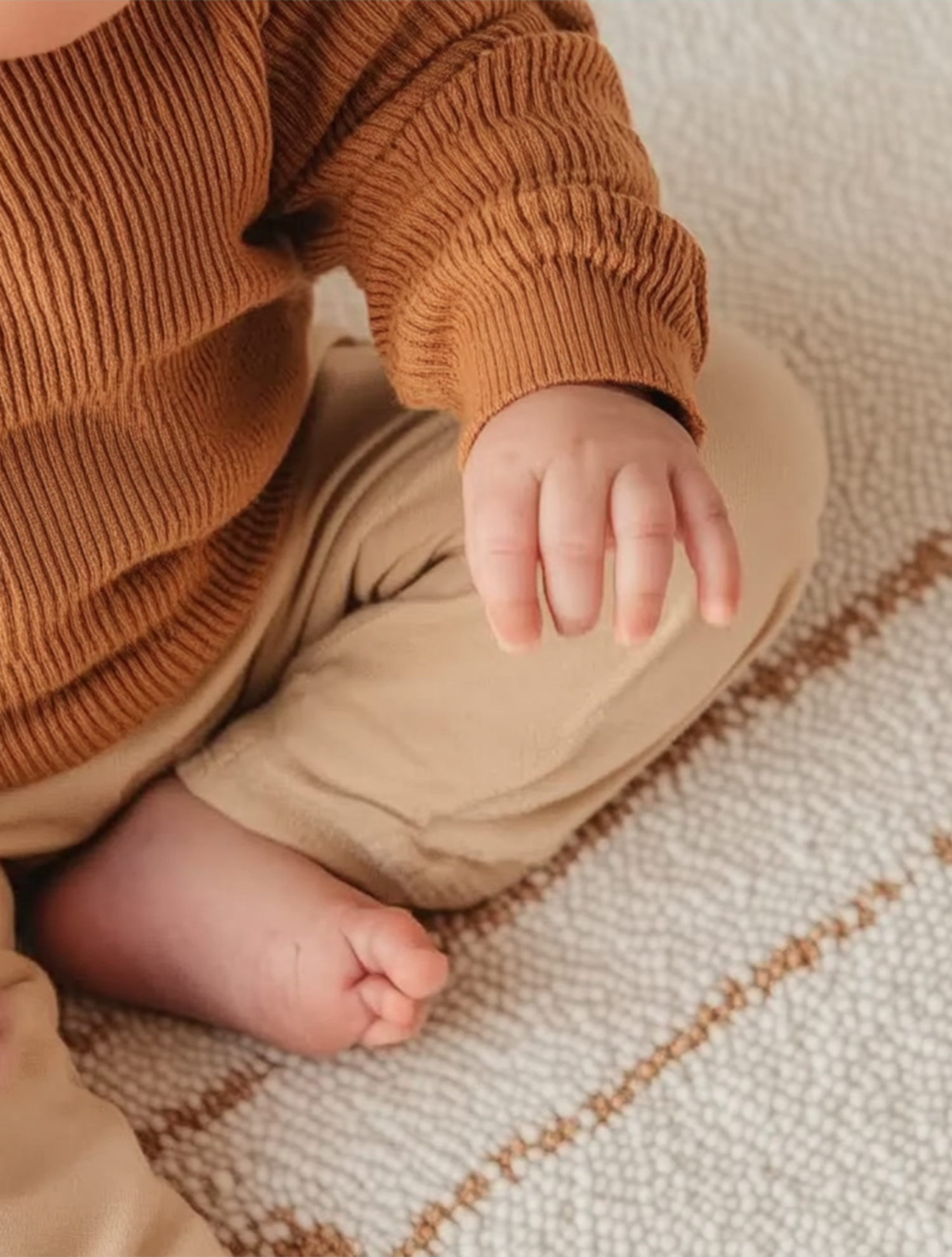 Soft textured rug with a minimal woven pattern, shown beneath a sitting baby in neutral-toned clothing to highlight the rug’s gentle and cozy surface.