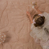 A child wearing a white lace fairy costume lies on a washable wool non-toxic children's rug.