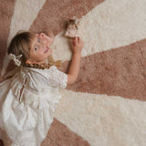 Child in a white dress lying on a large circular rug made with non-toxic, washable wool.