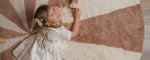 Child in a white dress lying on a large circular rug made with non-toxic, washable wool.