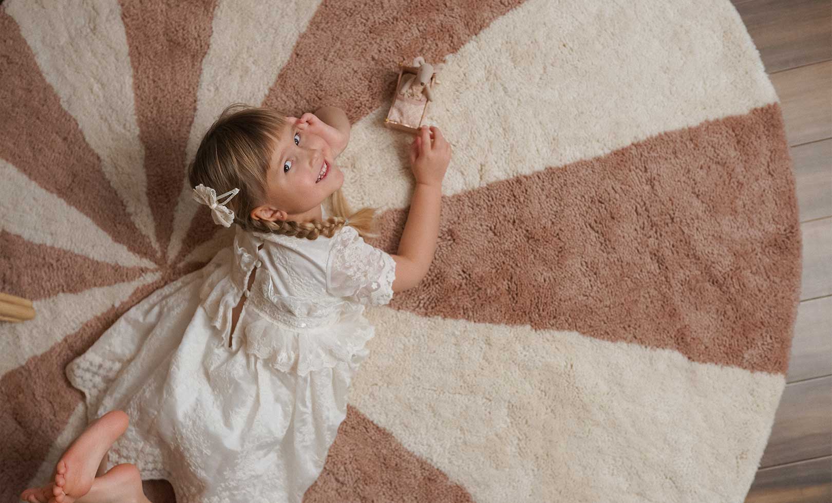 Child in a white dress lying on a large circular rug made with non-toxic, washable wool.