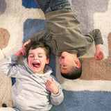 Child playing on a washable wool rug with a playful Tetris-inspired stacked pattern in earthy tones.