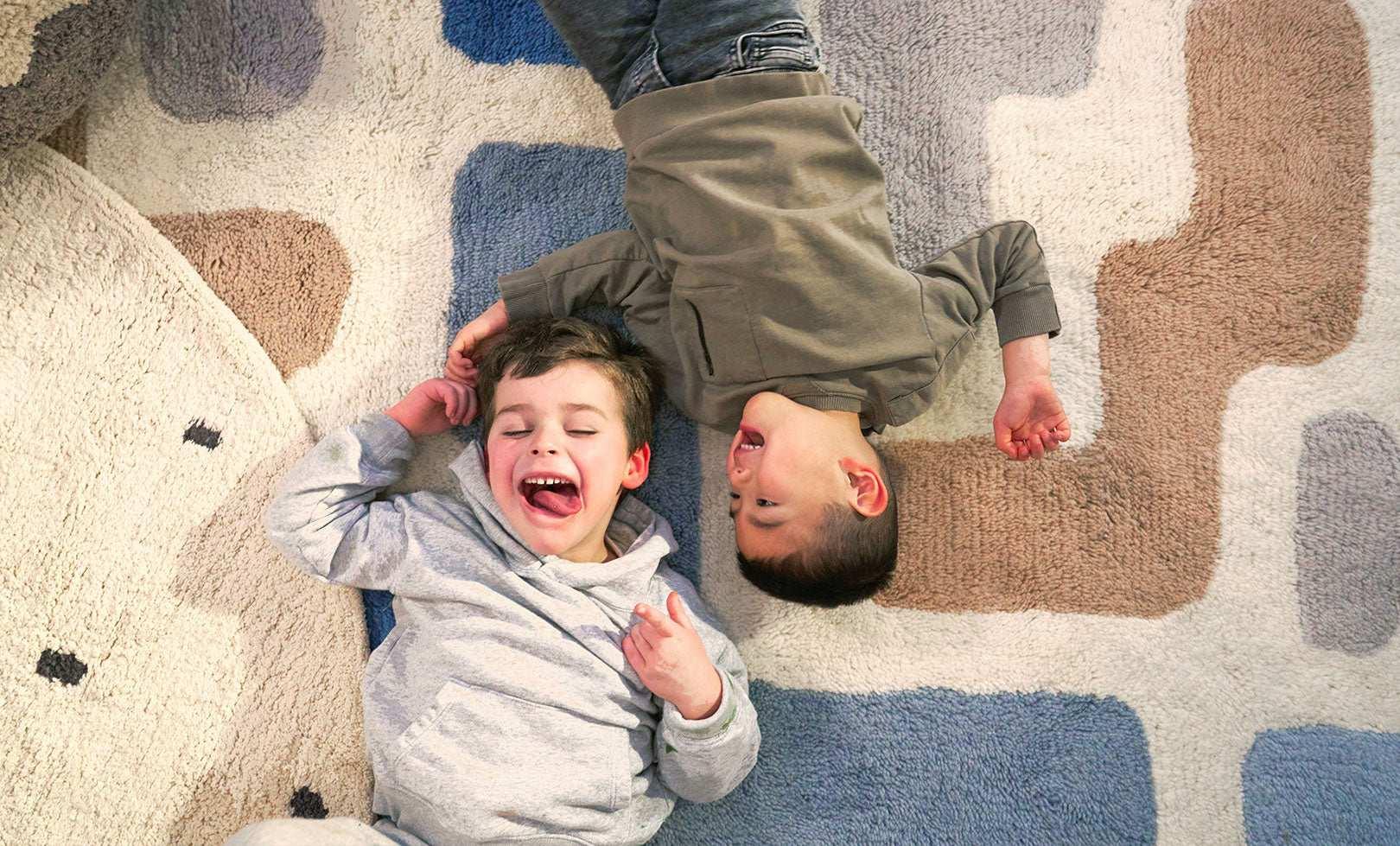 Child playing on a washable wool rug with a playful Tetris-inspired stacked pattern in earthy tones.